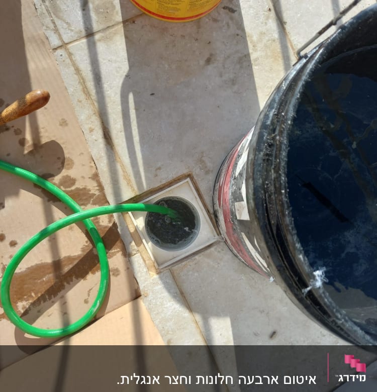 צינור ירוק בתוך פתח ניקוז עם דלי שחור